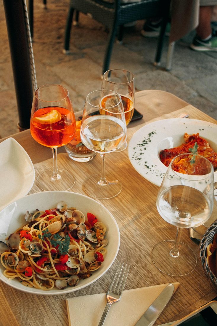 Terrastafel met een Aperol spritz, witte wijn, spaghetti alle vongole en een gegratineerd pastagerecht