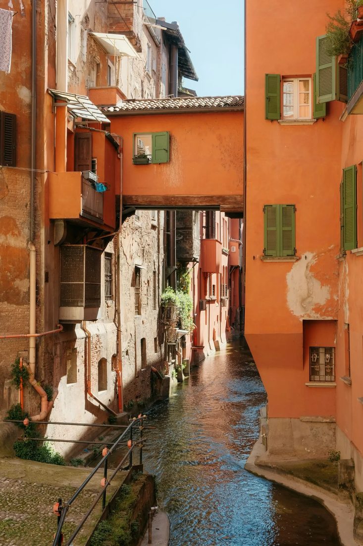 Smal kanaal tussen oranje gepleisterde huizen met groene luiken in Bologna