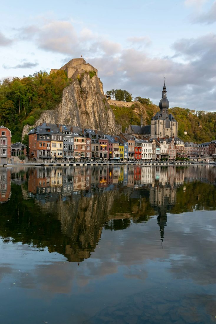 Kleurrijke huizen langs het water met een rotsklif en citadel erboven in de Belgische Ardennen