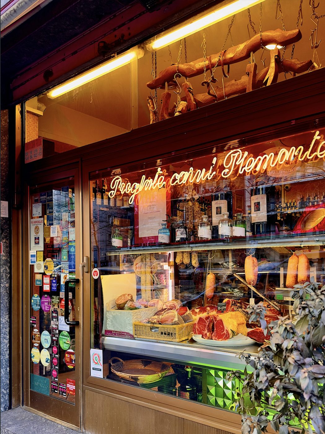 Warmly lit Italian deli with hams and cured meats in the window