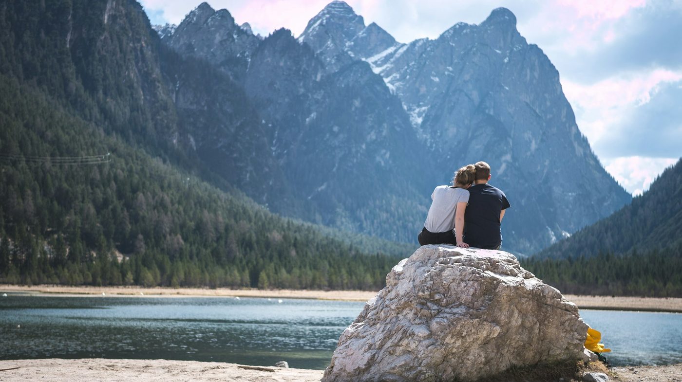 A couple sitting close together on a rock overlooking a mountain lake