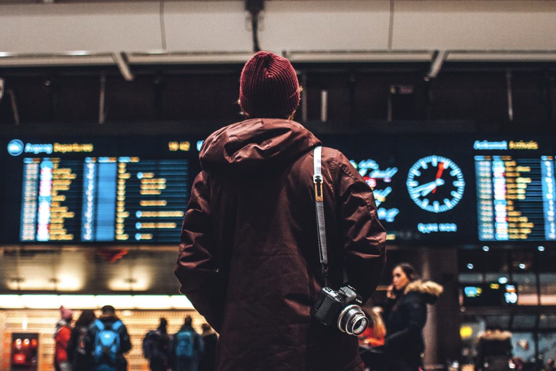 Reiziger met camera kijkt naar een verlicht vertrek- en aankomstbord in een stationshal