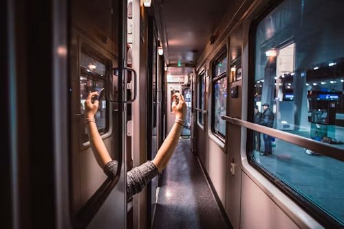 Twee armen steken uit het raam van een nachttrein op een verlicht perron