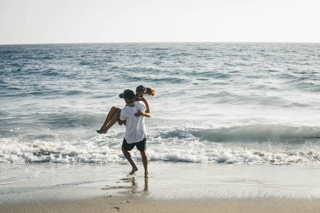 Man draagt een lachende vrouw door de branding op een zonnig strand