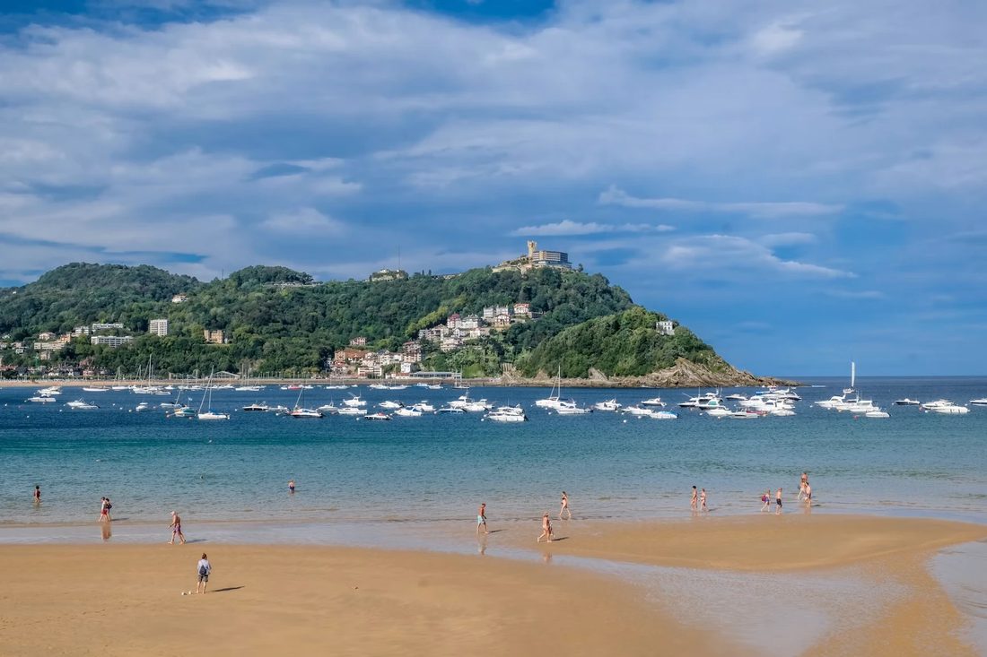 Het brede zandstrand van La Concha in San Sebastián met boten in de baai en een groene heuvel