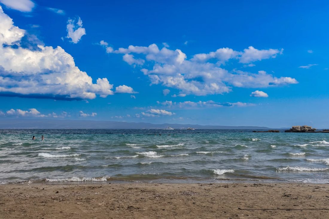 Zandstrand met helder water, lichte golven en een blauwe lucht met stapelwolken