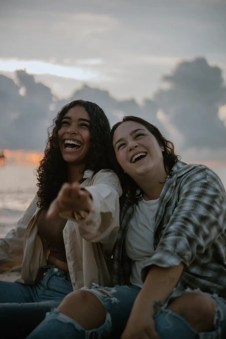 Twee lachende vriendinnen zitten samen op het strand in het laatste licht van de dag