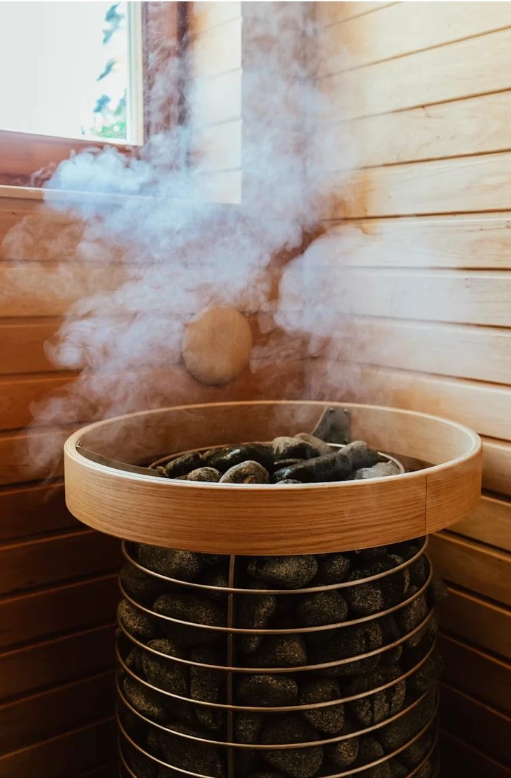 A sauna stove with hot stones giving off steam against a pale wooden wall