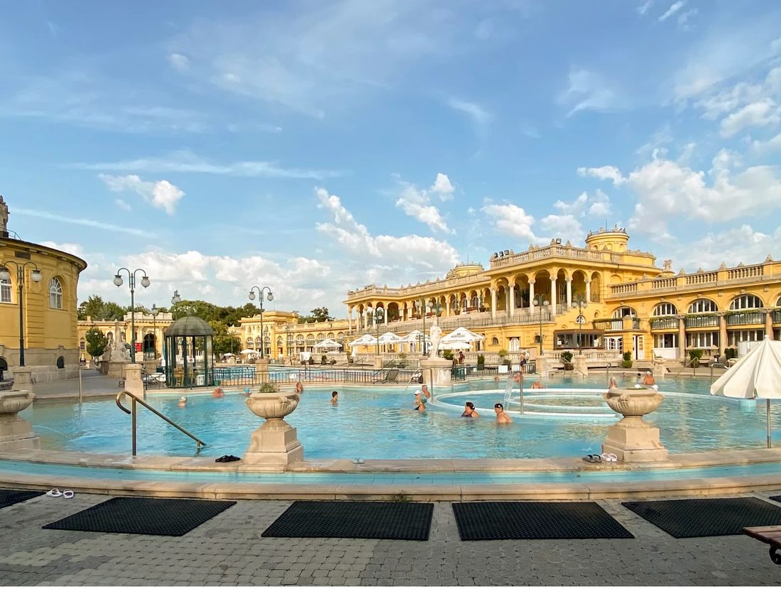 Outdoor thermal pools of a historic bathhouse with a yellow palace building and blue sky