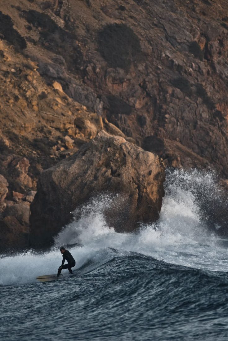 Surfer in wetsuit op een golf voor een rotsachtige kustwand