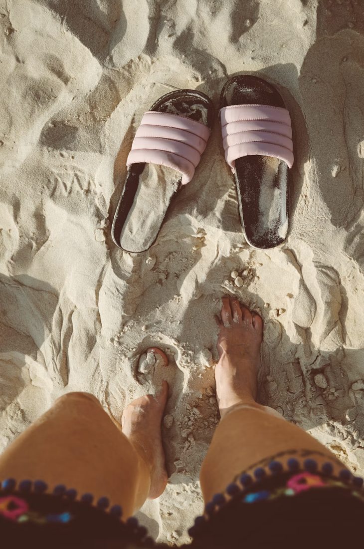 Blote voeten naast een paar roze slippers in warm, droog strandzand