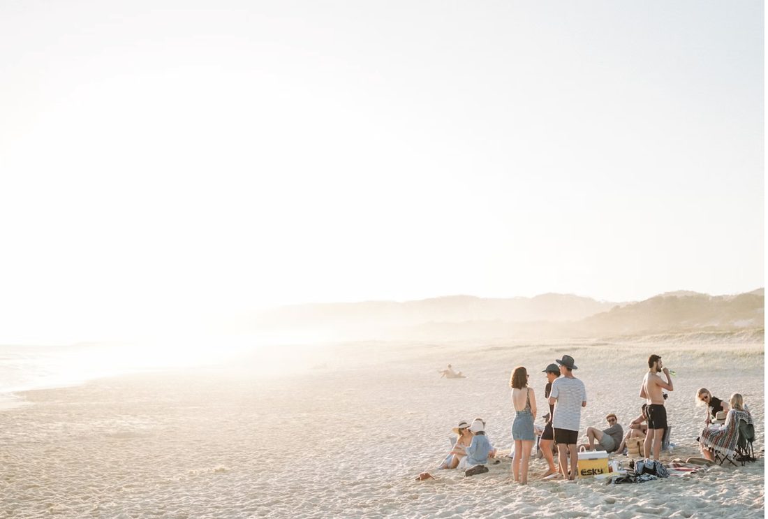 Groepje mensen bij het water op een breed, zonovergoten strand aan het eind van de middag